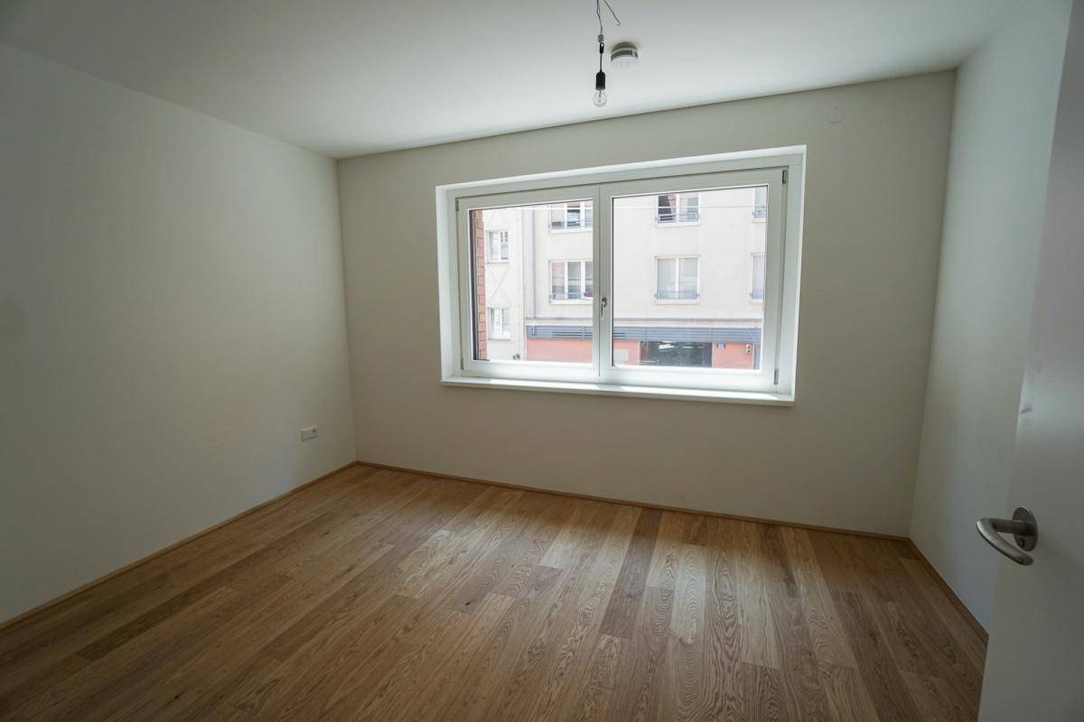 Helles Schlafzimmer mit einem großen Fenster und einem gepflegten Holzfußboden, bereit zur individuellen Gestaltung.
