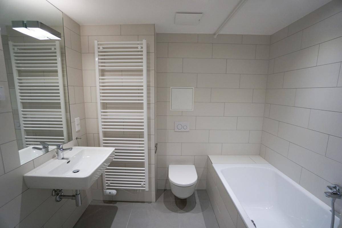 Modernes Badezimmer mit Badewanne, wandhängendem WC, Einzelwaschbecken und beheiztem Handtuchhalter.