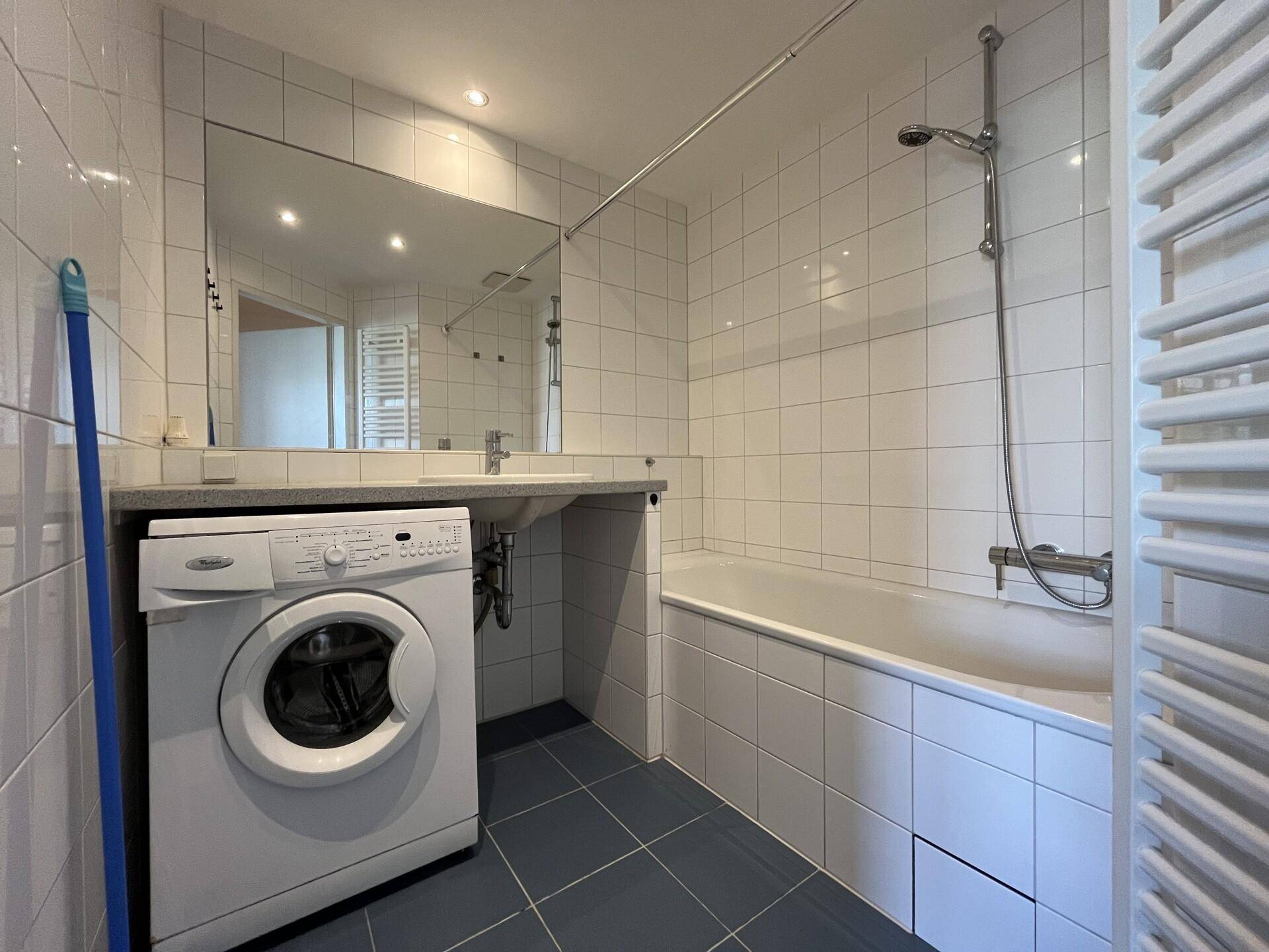 Gefliestes Badezimmer mit Badewanne, Duschvorrichtung, Waschbecken und Waschmaschine.