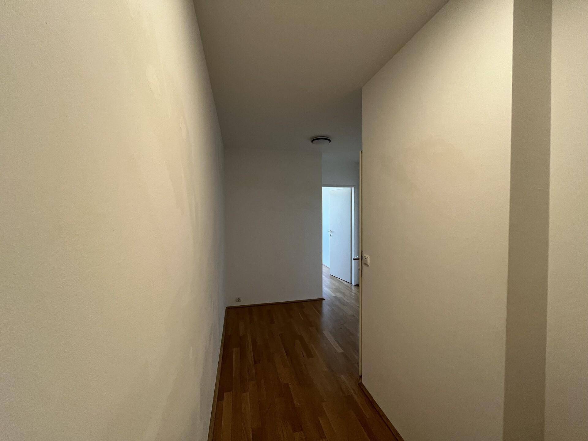 Langer, heller Flur mit Parkettboden, der zu weiteren Räumen in der Wohnung führt.