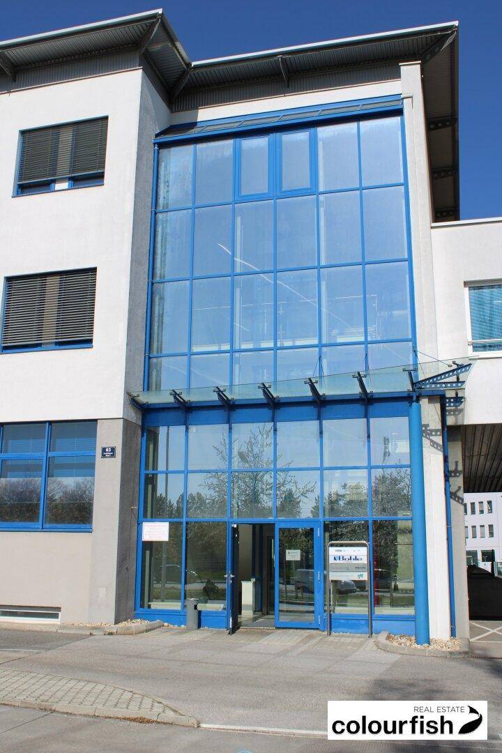 Detaillierte Ansicht des Haupteingangs mit großer Glasfront und blauen Akzenten unter klarem Himmel.