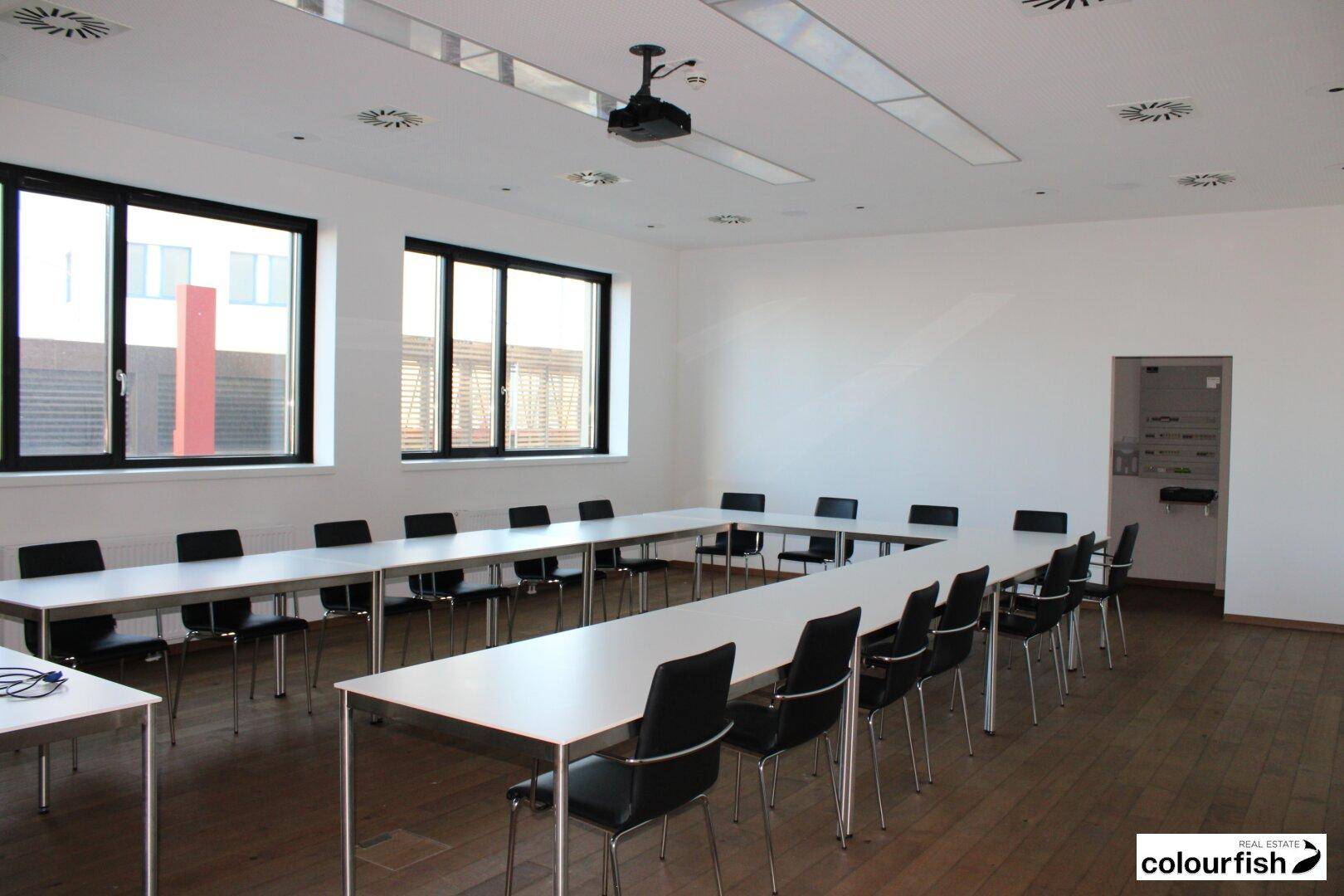 Heller Konferenzraum mit U-förmiger Tischordnung, bequemen Stühlen und einem Deckenprojektor für Präsentationen.