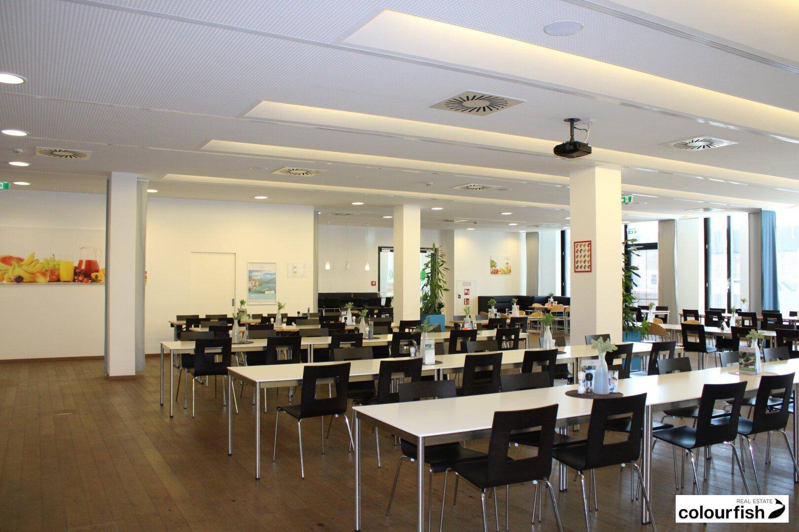 Geräumiger, moderner Speisesaal mit vielen Tischen und Stühlen, ideal für eine Kantine oder ein Restaurant.