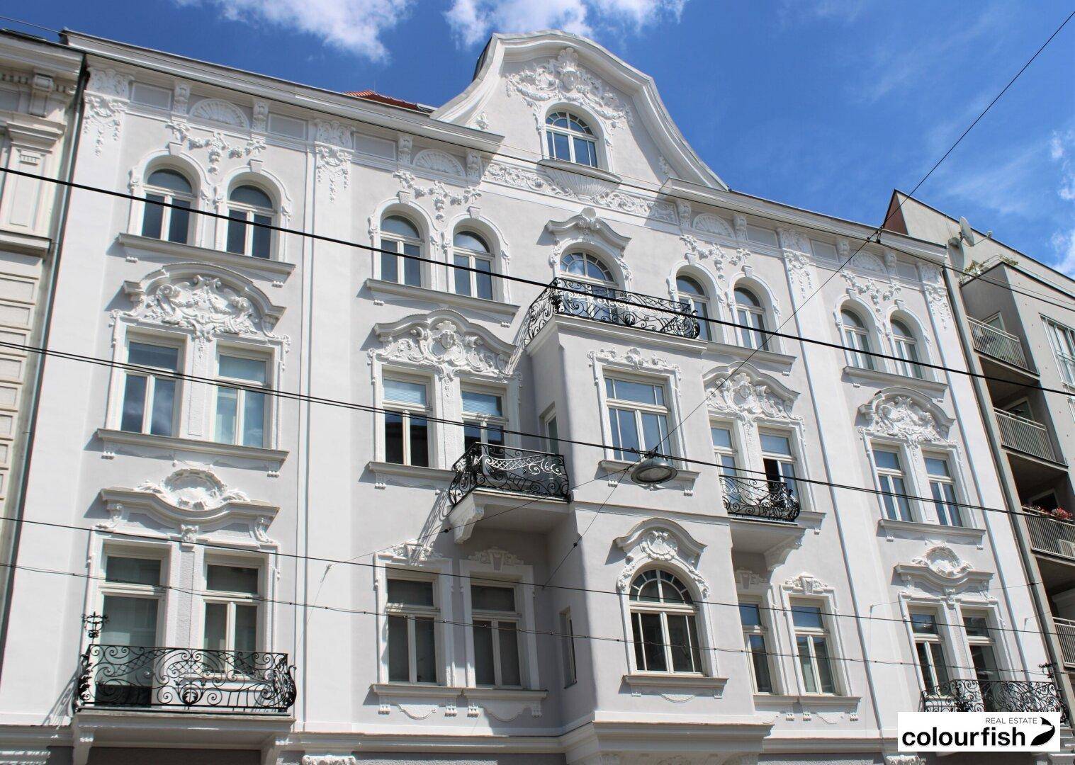 Historische Fassade eines Altbaus mit reich verzierten Stuckelementen und schmiedeeisernen Balkonen.