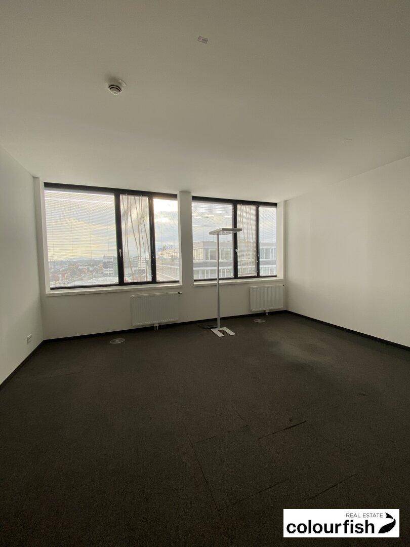 Heller, leerer Büroraum mit großen Fenstern, die einen weiten Blick über die Stadt bieten.