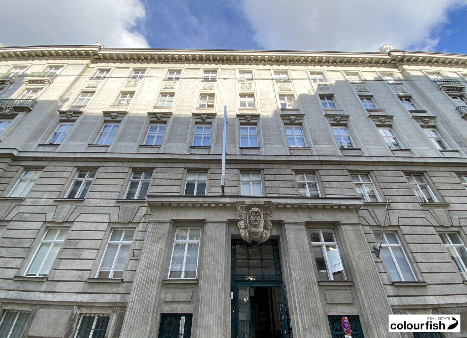 Großes, klassisches Gebäude mit vielen Fenstern und einer verzierten Fassade unter bewölktem Himmel.