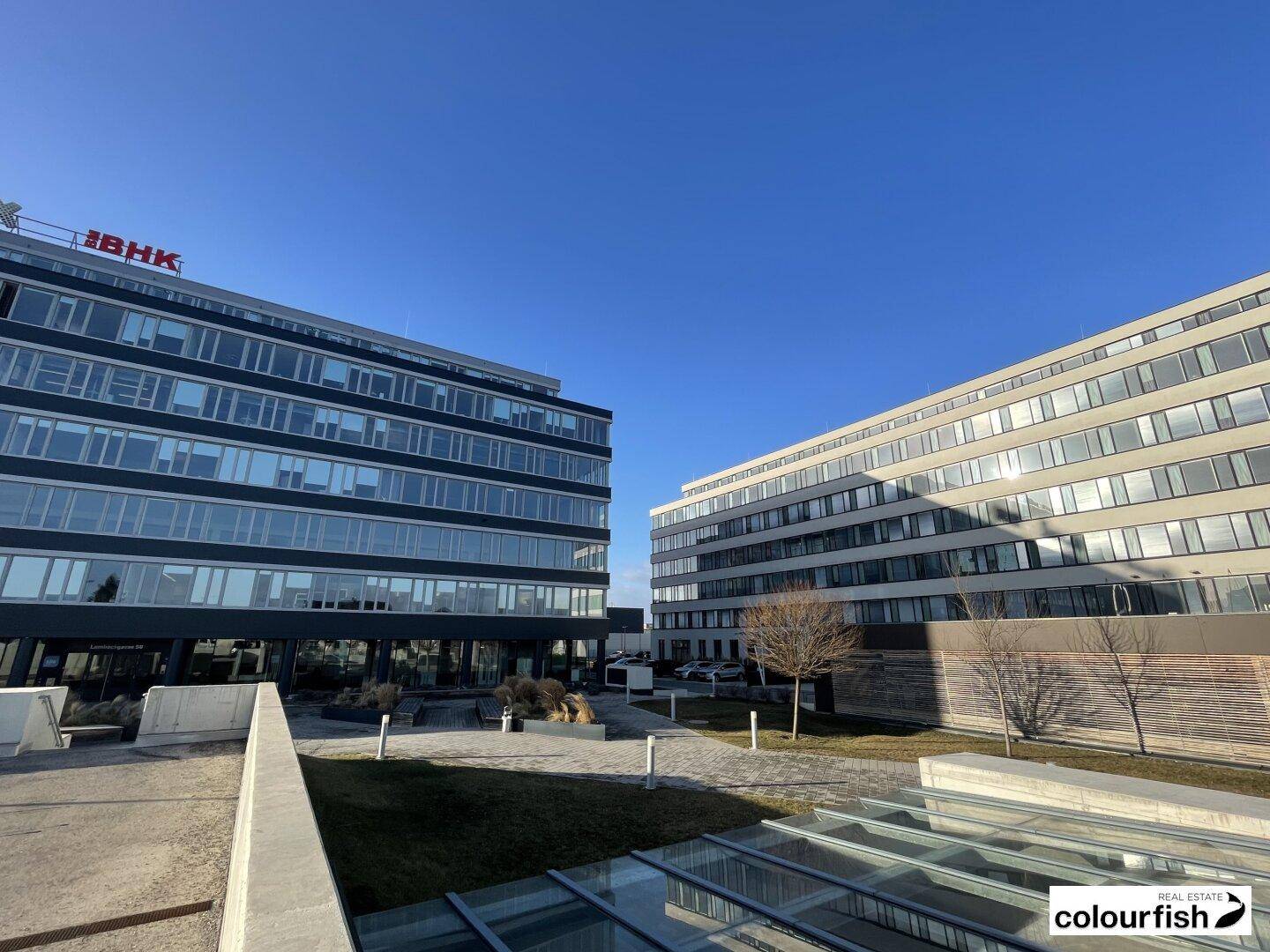Zwei moderne Bürogebäude mit großen Fensterfronten unter klarem blauem Himmel.