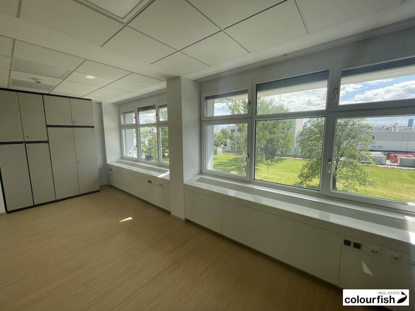 Helles, leeres Büro mit großen Fenstern, Blick ins Grüne und integrierten Schränken.