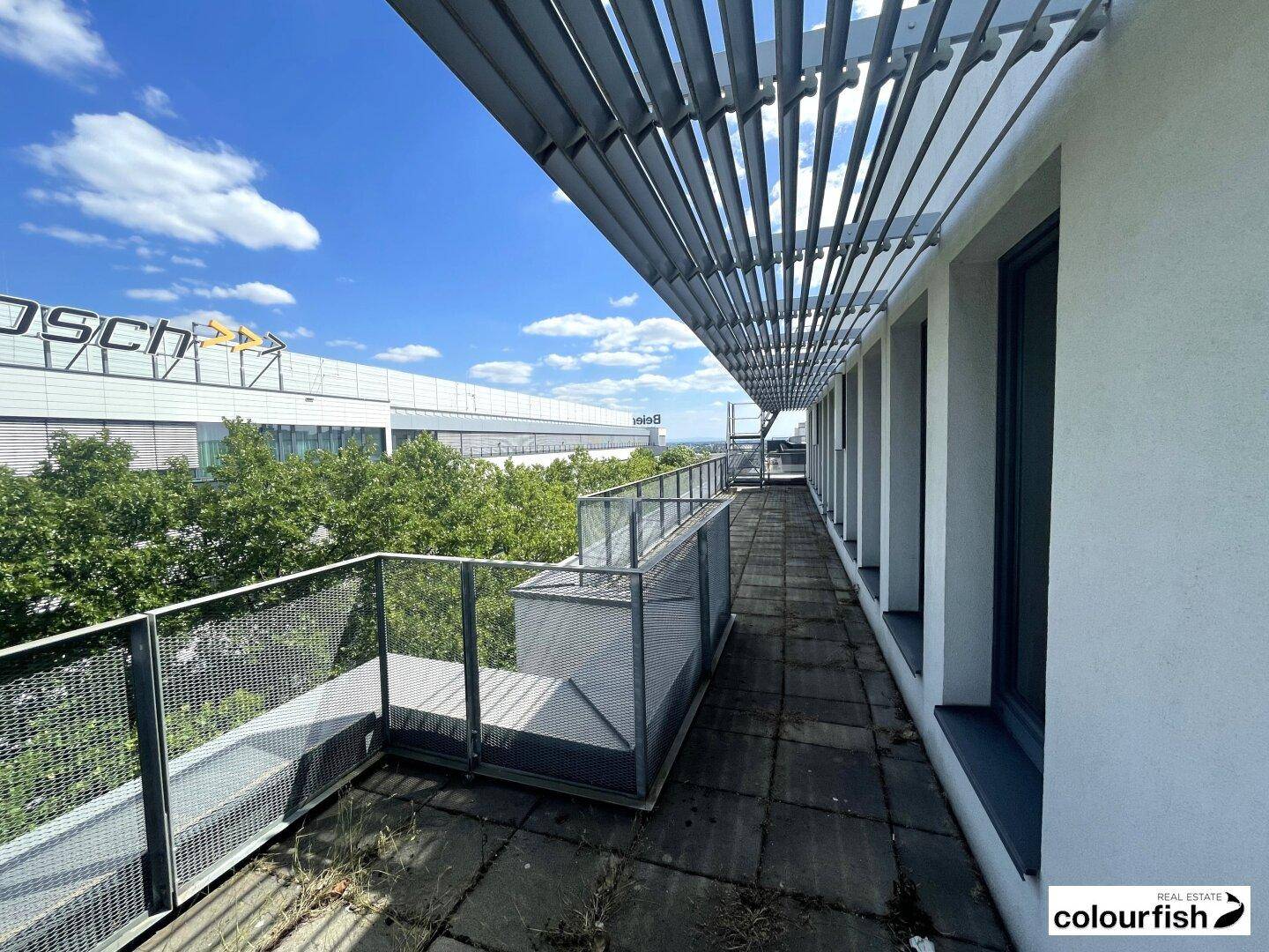 Geräumige Terrasse mit Metallgeländer und Blick auf grüne Bäume und Industriegebäude.