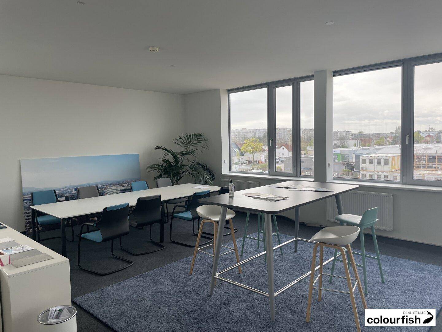Moderner Bürobereich mit hohen Tischen, Barhockern und großen Fenstern mit Stadtblick.