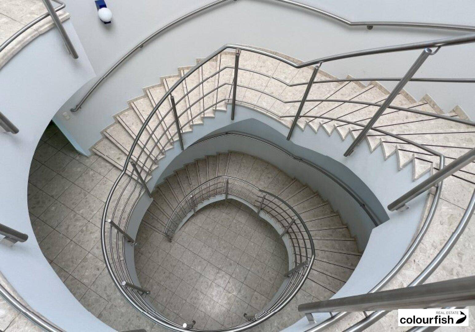 Elegante Wendeltreppe mit Edelstahlgeländer und Fliesenboden, die mehrere Etagen verbindet.