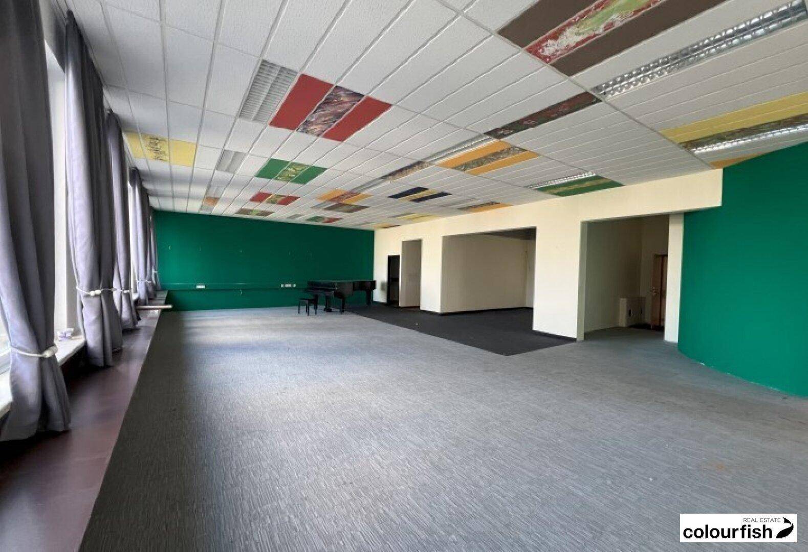 Großer Büroraum mit grün gestrichenen Wänden, Teppichboden und farbigen Deckenplatten.