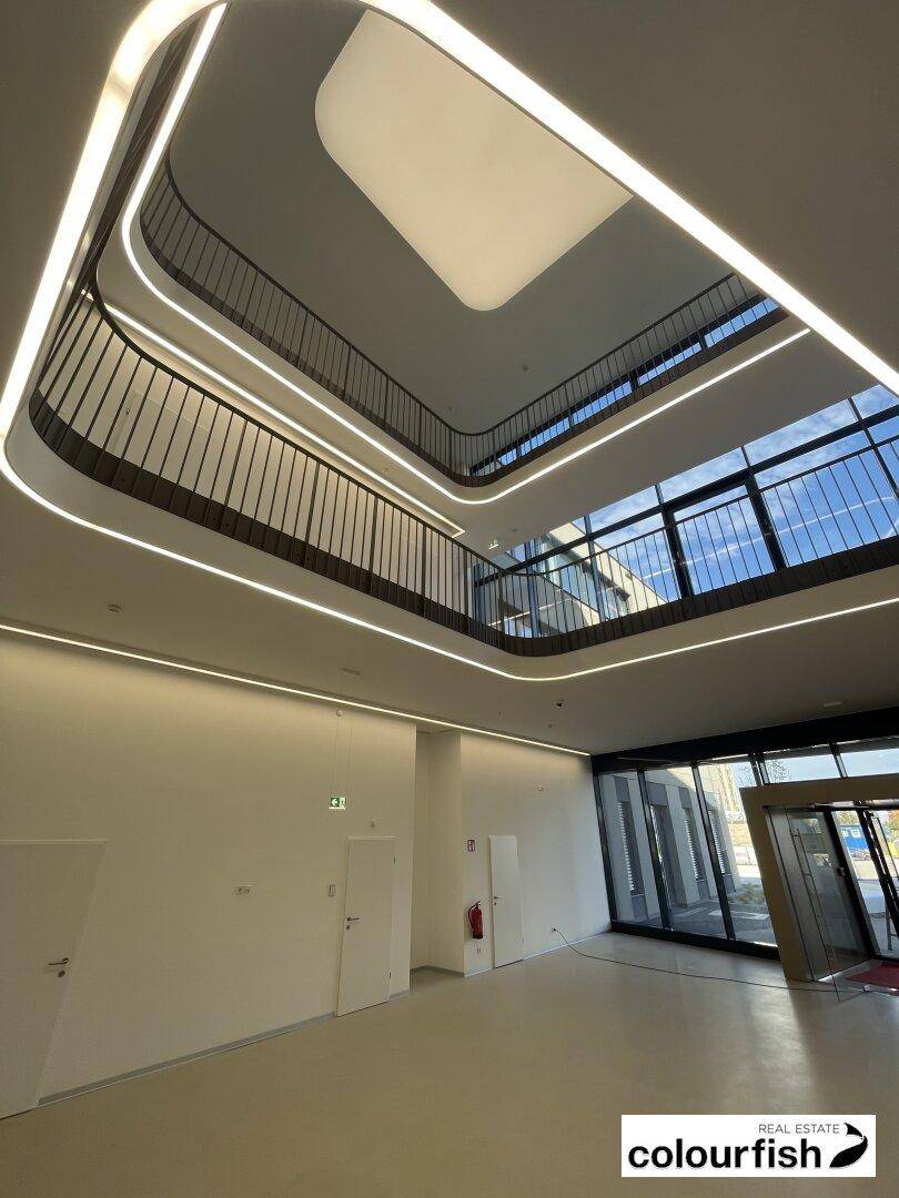 Modernes, mehrstöckiges Foyer mit viel Tageslicht, eleganten Geländern und integrierter Beleuchtung.