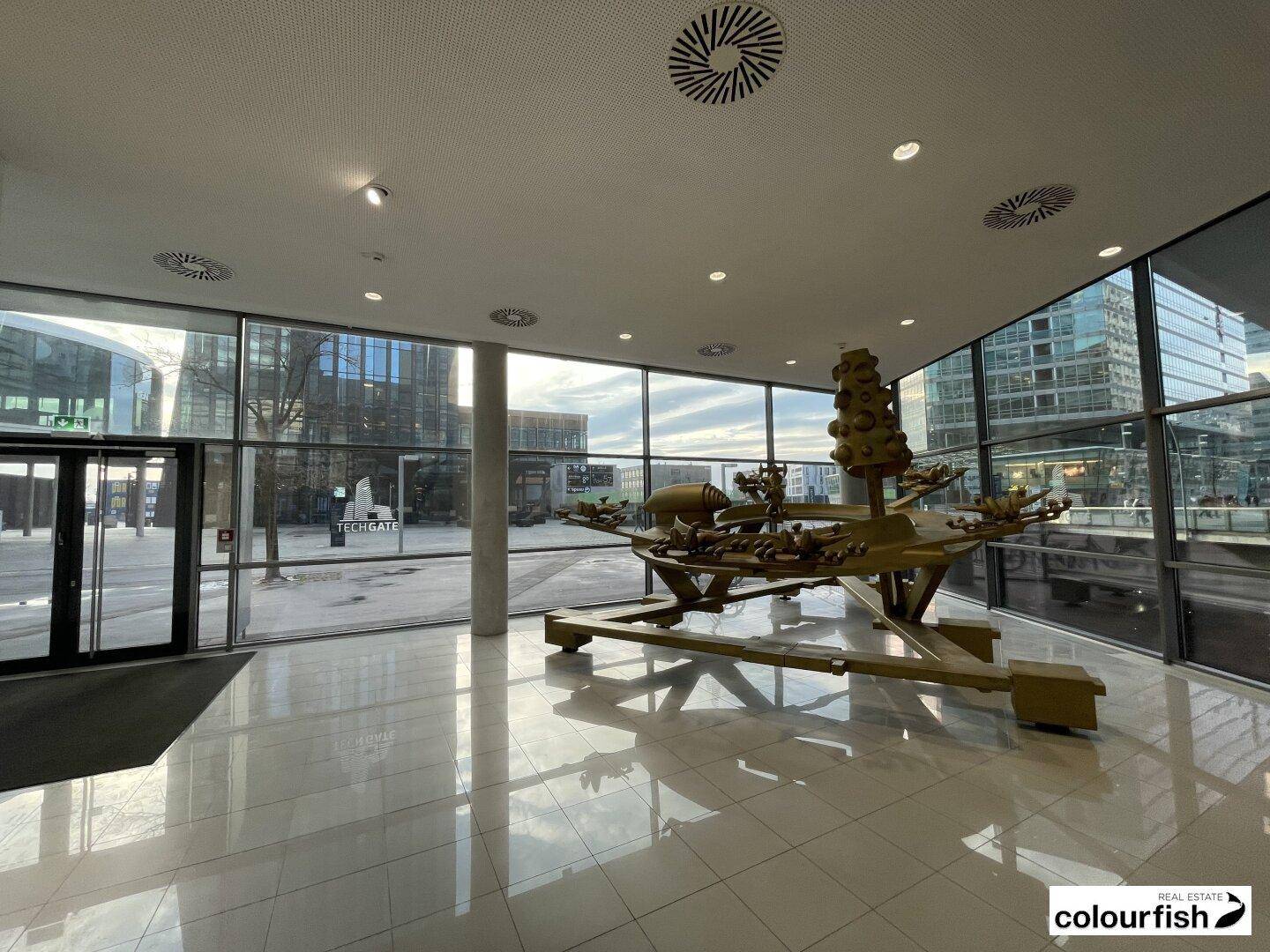 Helle und geräumige Lobby mit großen Glasfenstern und einer modernen Skulptur in der Mitte.