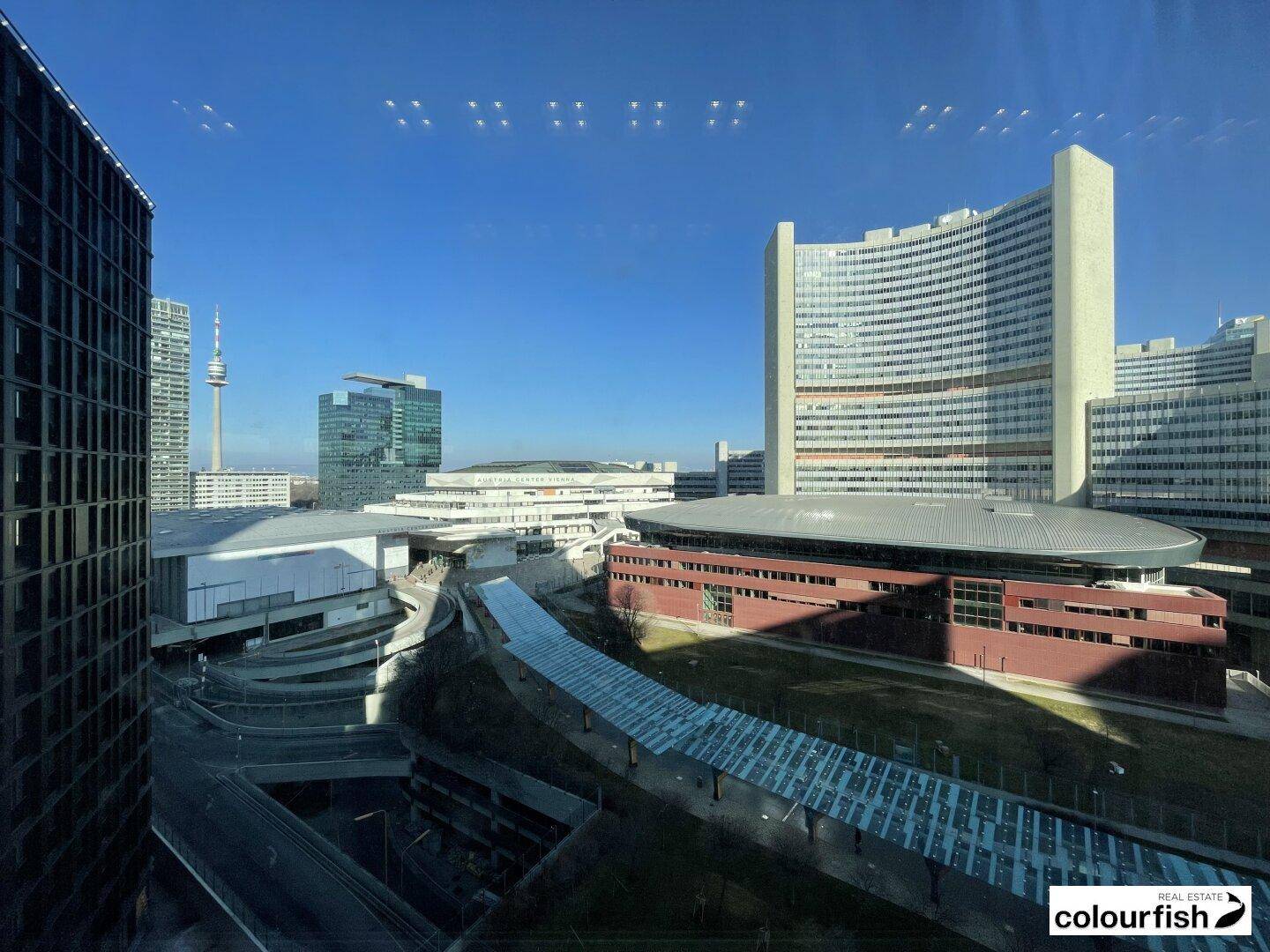 Weitläufiger Blick aus dem Fenster auf die moderne Stadtlandschaft mit markanten Gebäuden und blauem Himmel.