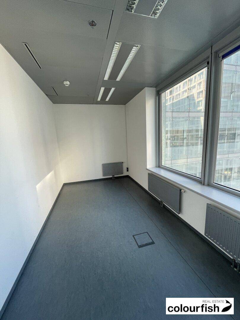 Kompaktes Büro mit dunklem Bodenbelag und Fenstern, die für ausreichend Tageslicht sorgen.