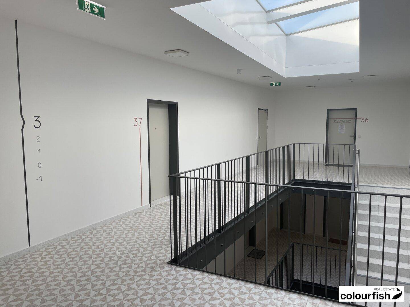 Heller Treppenhausbereich mit modernem Geländer, geometrischem Fliesenboden und Oberlicht für natürliches Licht.