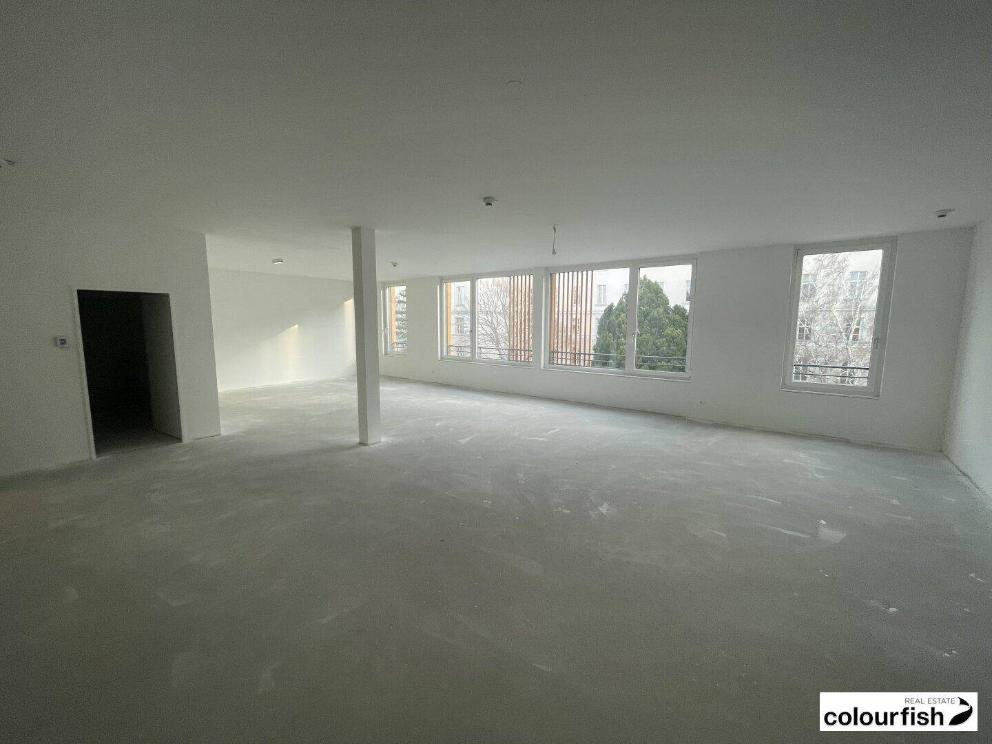 Großer, leerer Gewerberaum mit vielen Fenstern und Betonboden, bereit für den Innenausbau.