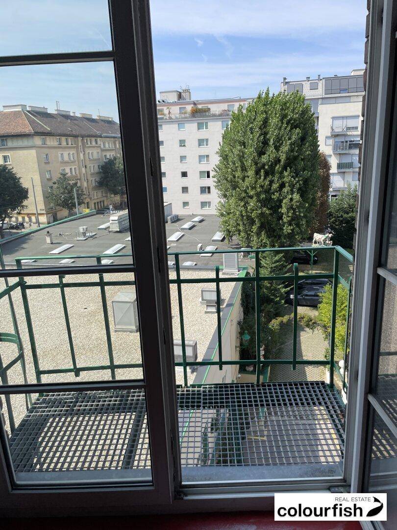 Balkon mit Gitterboden und Blick auf die Dächer der Stadt und umliegende Gebäude unter blauem Himmel.