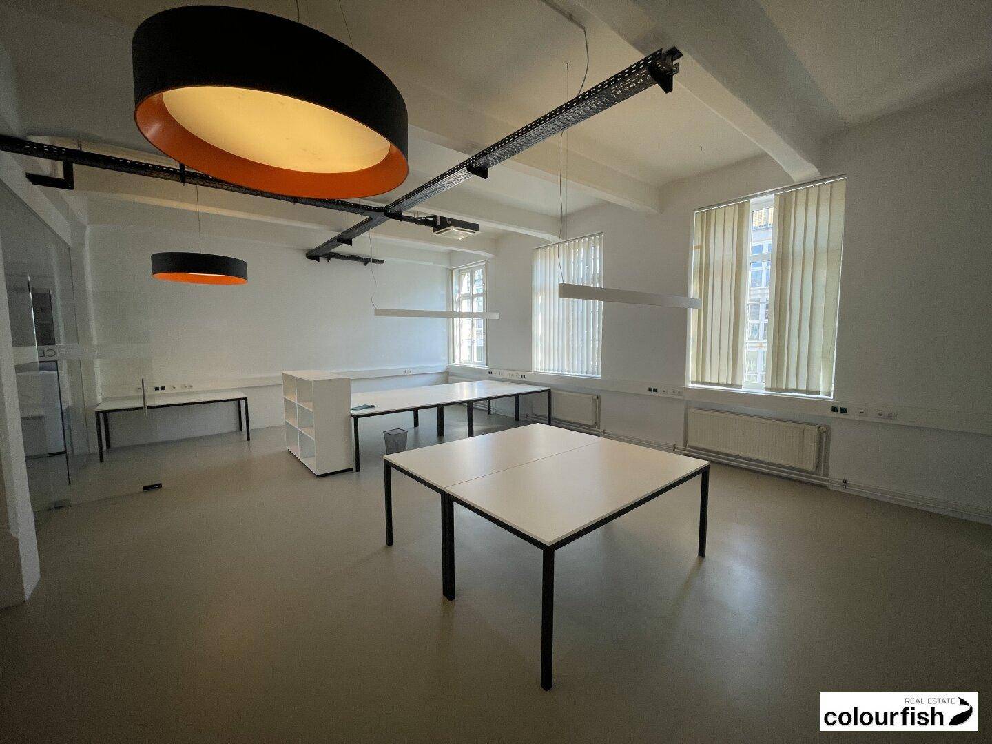 Weitläufiges Büro mit großen Fenstern, modernen Schreibtischen und auffälligen runden Deckenleuchten.