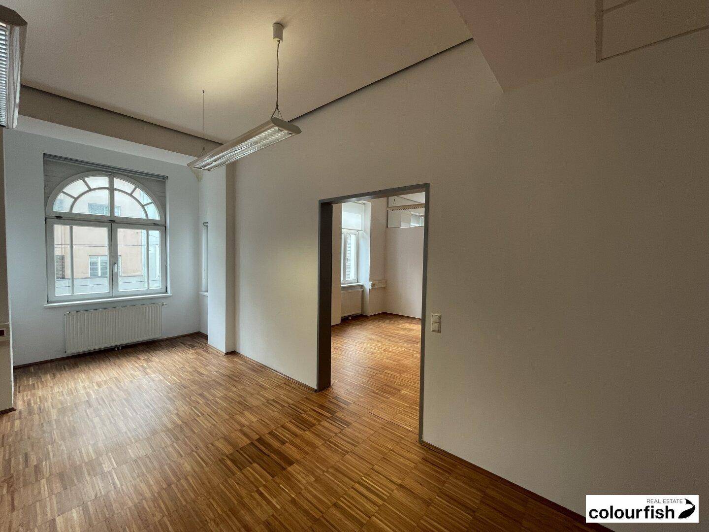 Großer, heller Büroraum mit Holzboden und einem eleganten Rundbogenfenster, das viel Licht spendet.