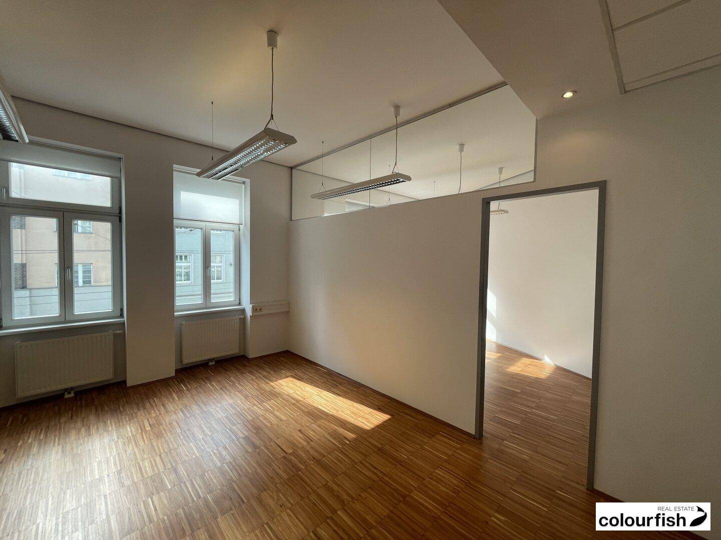 Heller Büroraum mit Holzboden und einer modernen Trennwand, die den Raum unterteilt.
