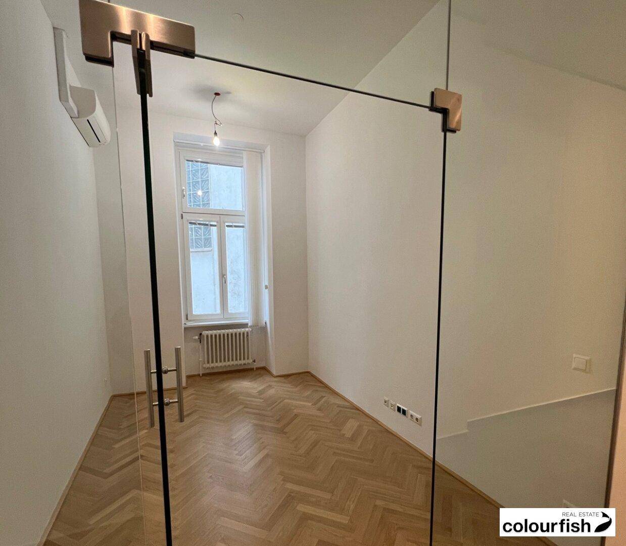 Büro mit Fischgrätparkett, einem Fenster und modernen Glaswänden, ausgestattet mit Klimaanlage.