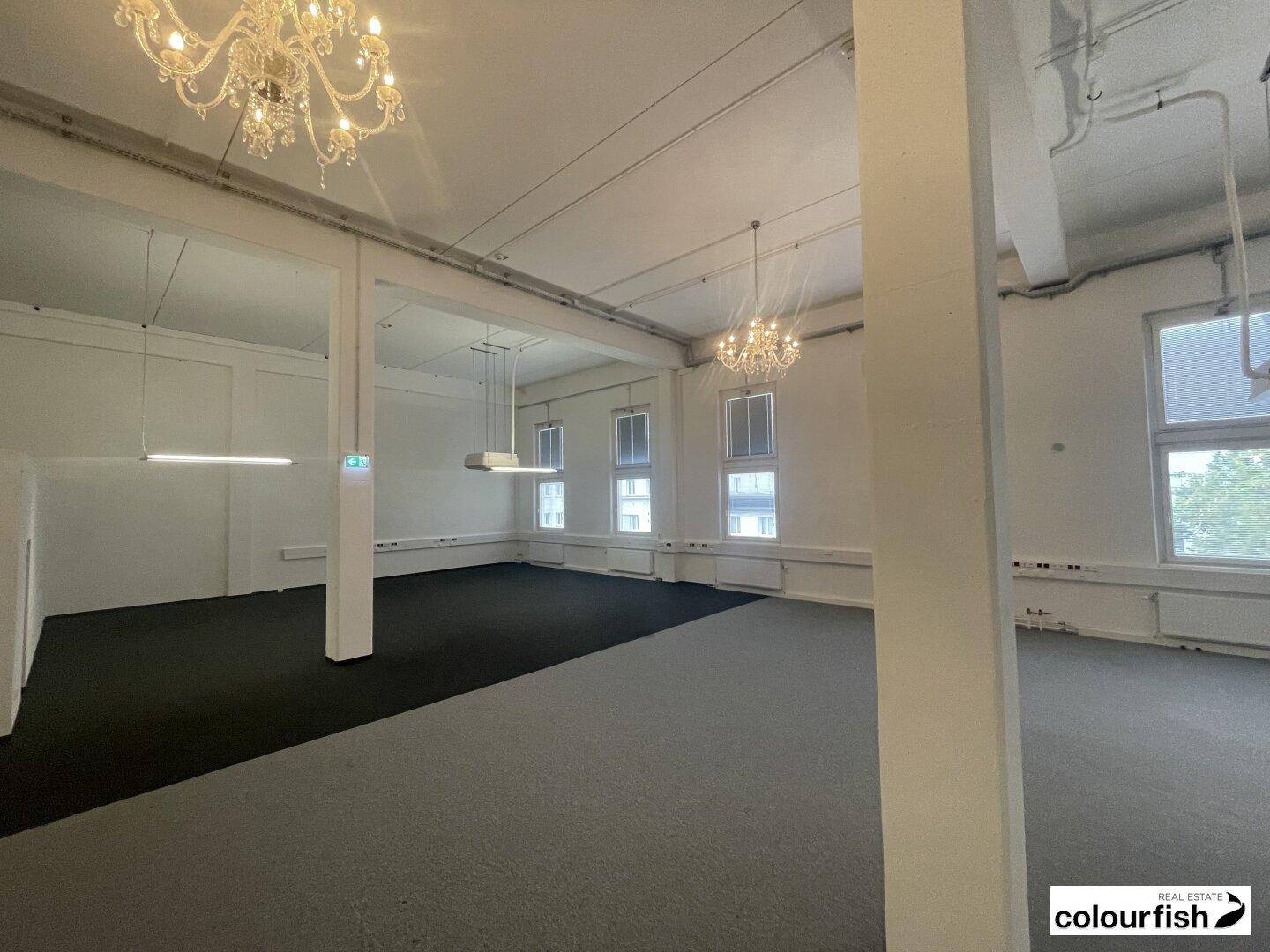 Großer, offener Bürobereich mit Säulen, Teppichboden und dekorativen Kronleuchtern an der Decke.