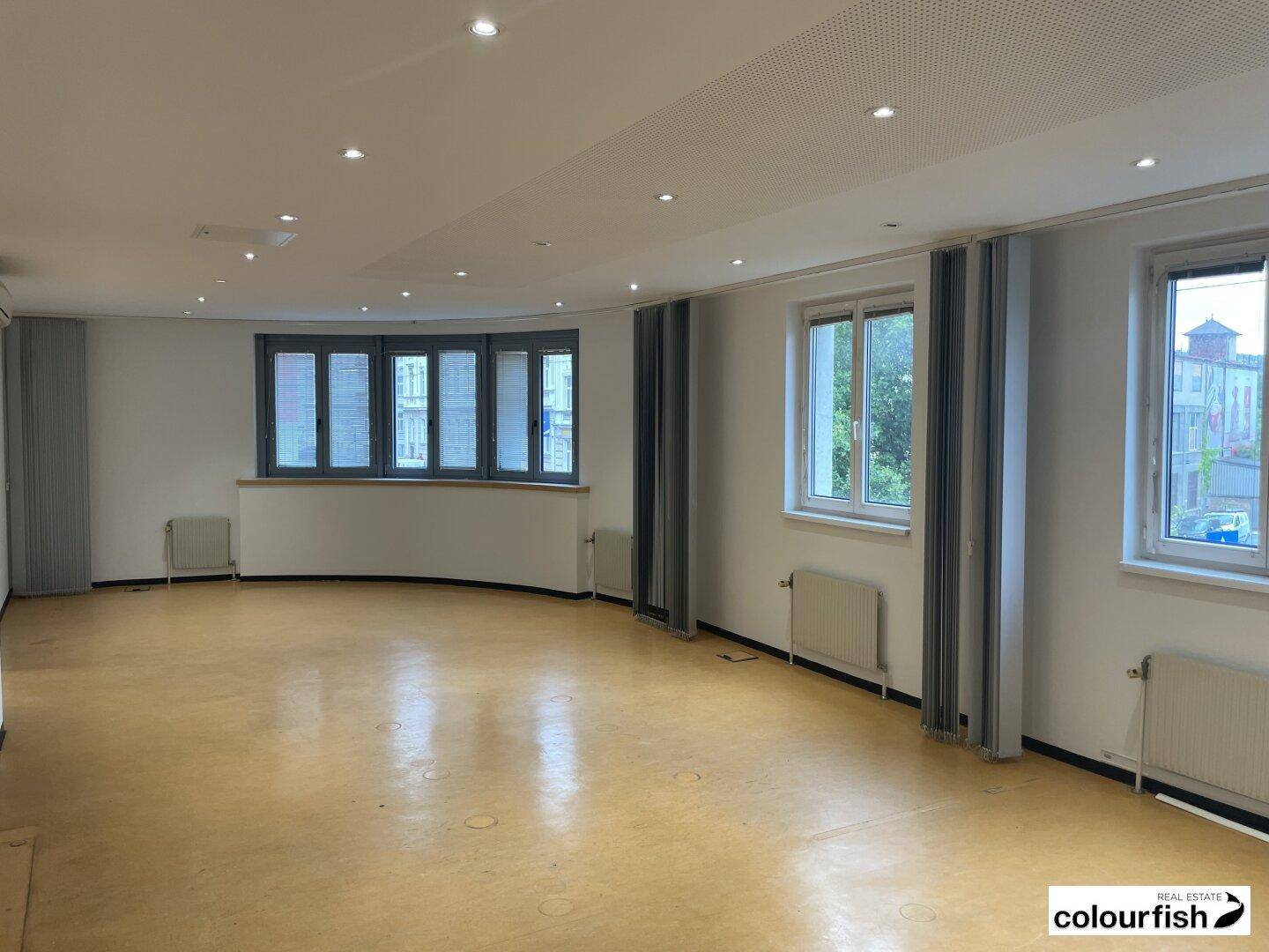 Großes, leeres Büro mit vielen Fenstern, Heizkörpern und einem abgehängten Deckenraster, bereit zur Einrichtung.