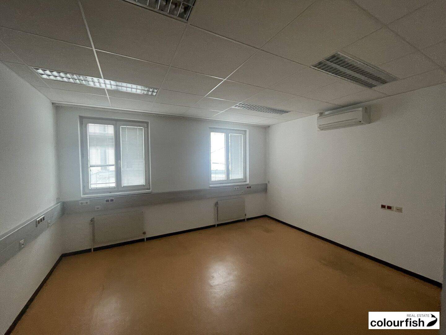 Helles Bürozimmer mit zwei Fenstern, Heizkörpern und Klimaanlage, bereit für die individuelle Gestaltung.