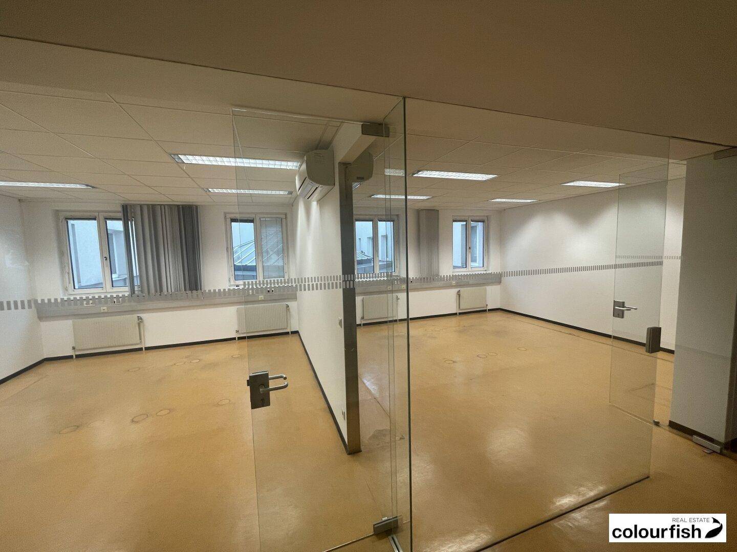 Offener Bürobereich mit Glaswänden, vielen Fenstern und Klimaanlagen, ideal für moderne Arbeitskonzepte.