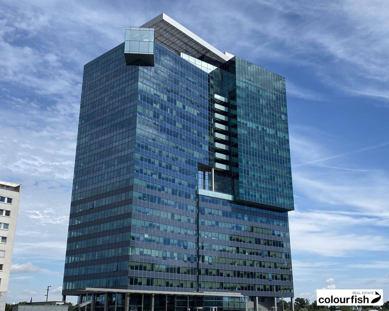 Ein modernes Hochhaus mit einer beeindruckenden Glasfassade und Solarpaneelen auf dem Dach unter blauem Himmel.