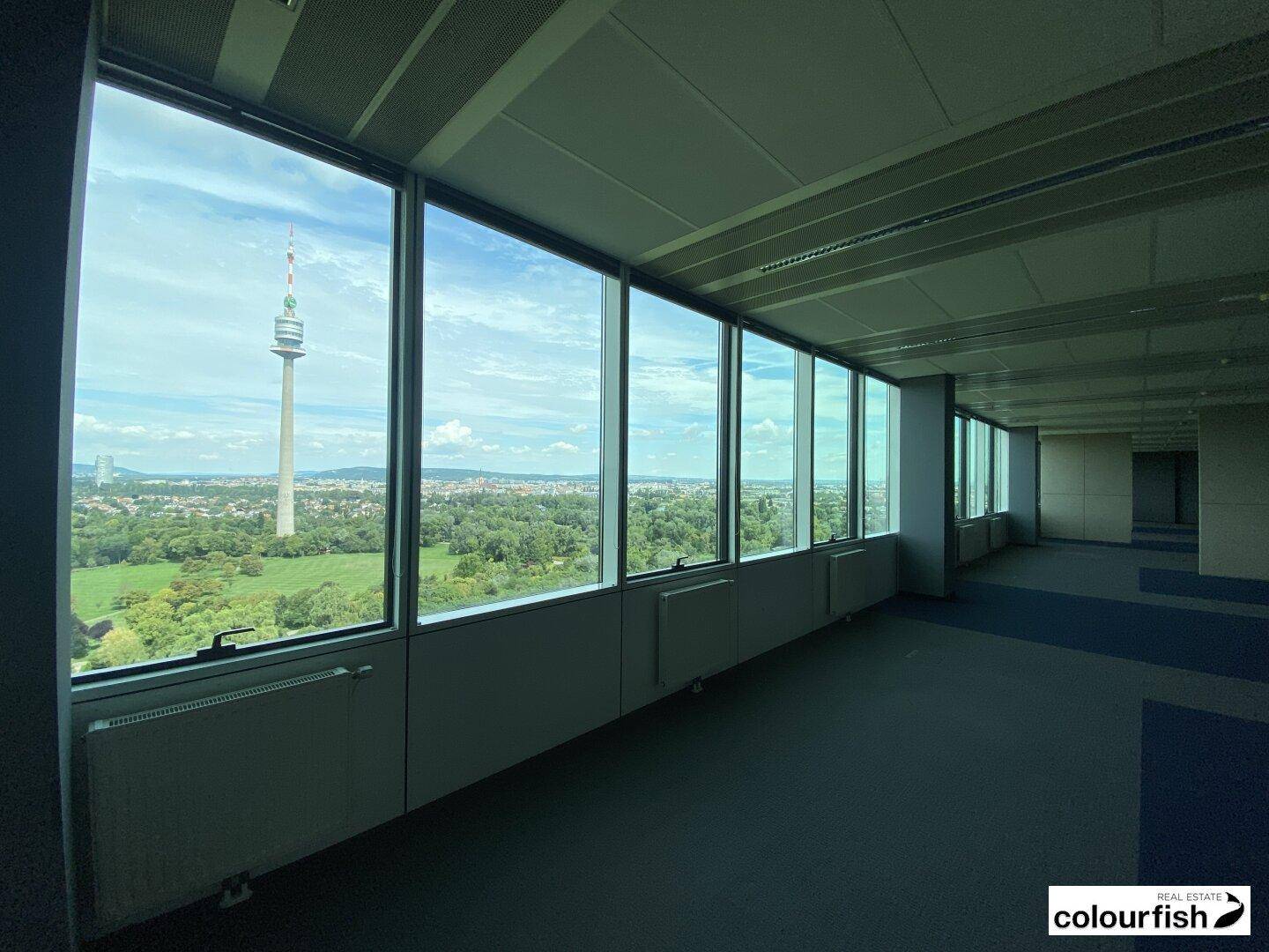 Langer Bürobereich mit vielen Fenstern, die viel Tageslicht hereinlassen und einen Blick auf die Stadt bieten.