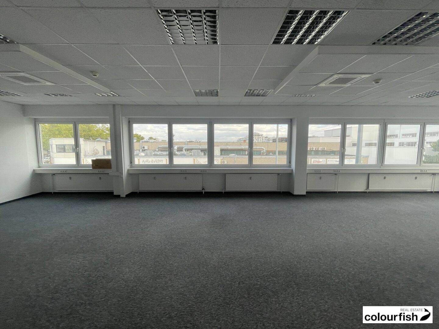 Weitläufiges Büro mit durchgehenden Fenstern, die für eine helle und offene Arbeitsatmosphäre sorgen.