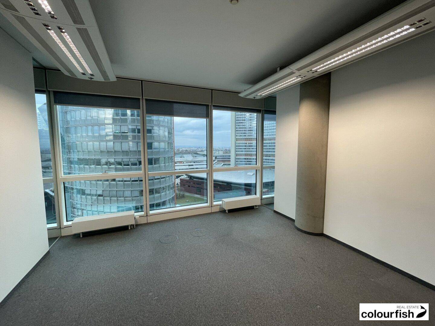 Bürofläche mit Teppichboden und raumhohen Fenstern, die eine weite Aussicht auf die Stadt bieten.