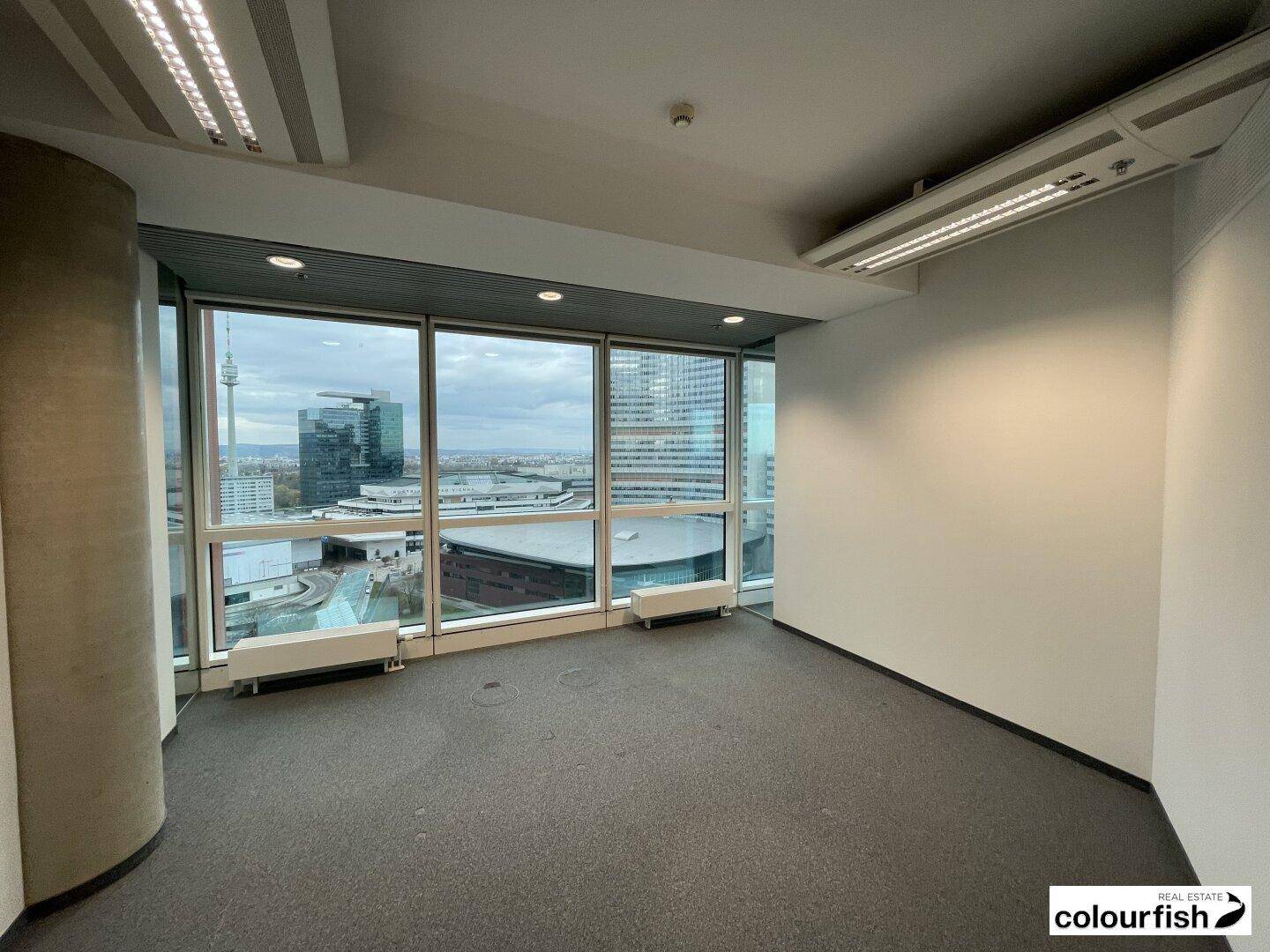 Eckbüro mit Teppichboden und großen Fenstern, die einen weiten Blick über die Stadtlandschaft bieten.