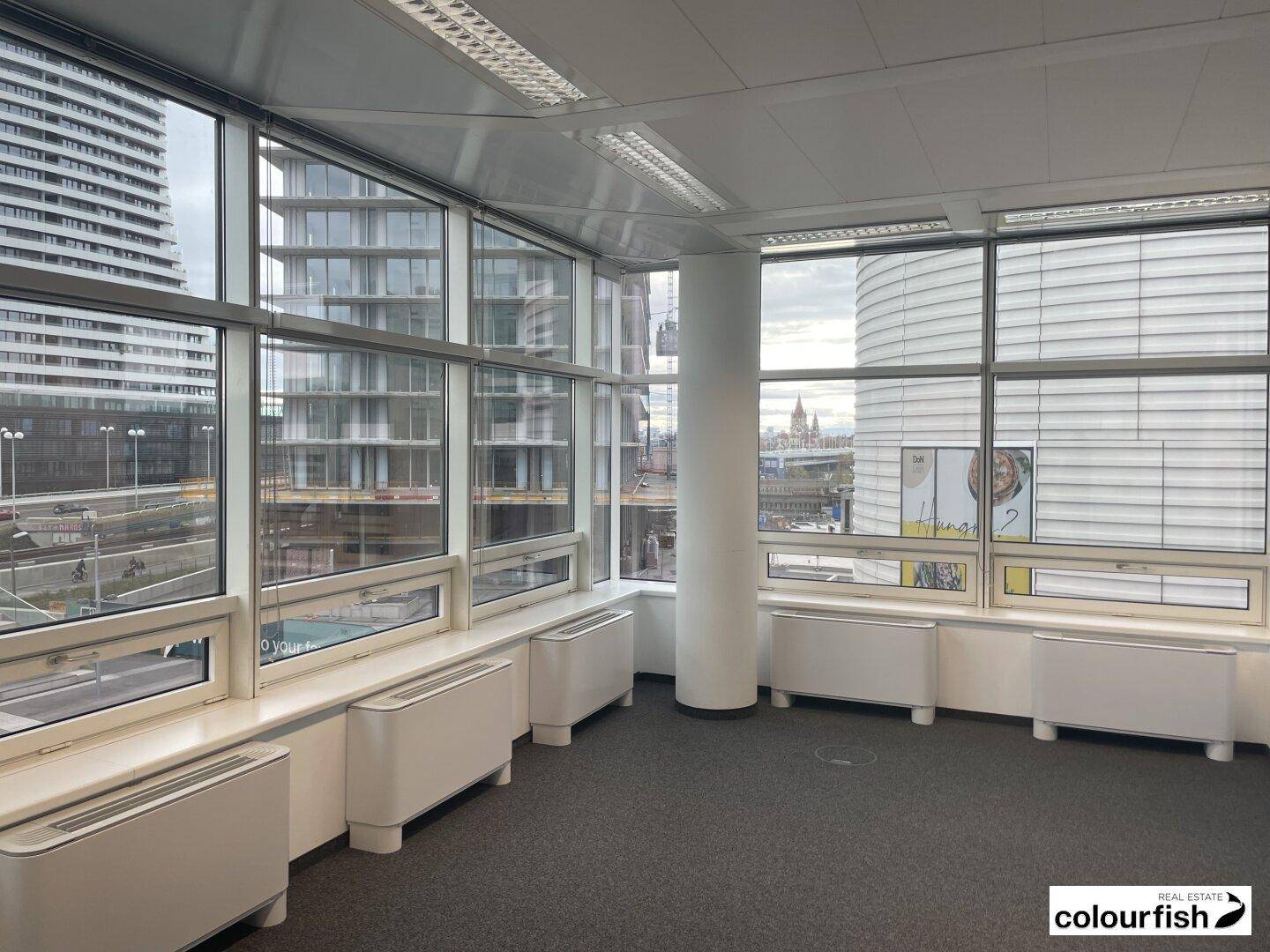 Helles Eckbüro mit weitreichenden Fenstern, die einen Panoramablick auf die Stadt und andere Gebäude bieten.