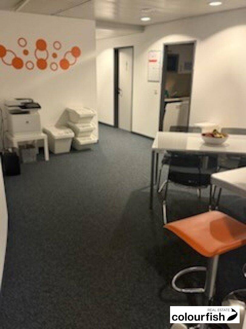 Bürobereich mit Teppichboden, Druckern und einem Tisch mit Stühlen, ideal für Teamarbeit.