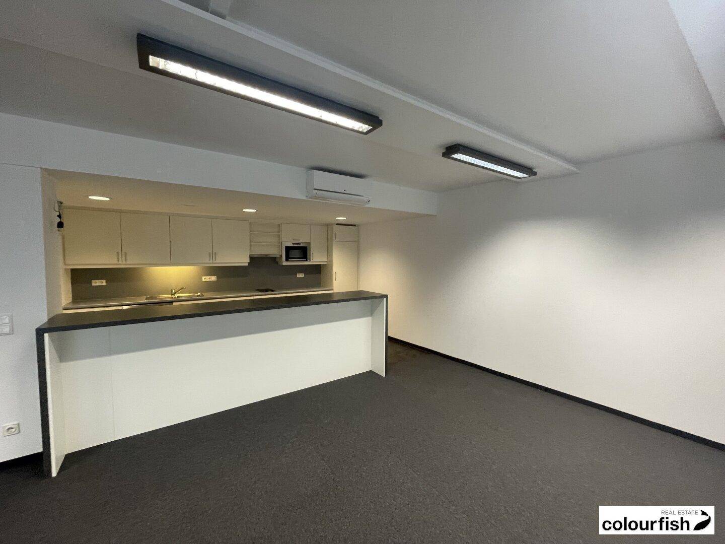 Moderne Teeküche in einem Büroraum mit Einbauschränken, Spüle und Mikrowelle.