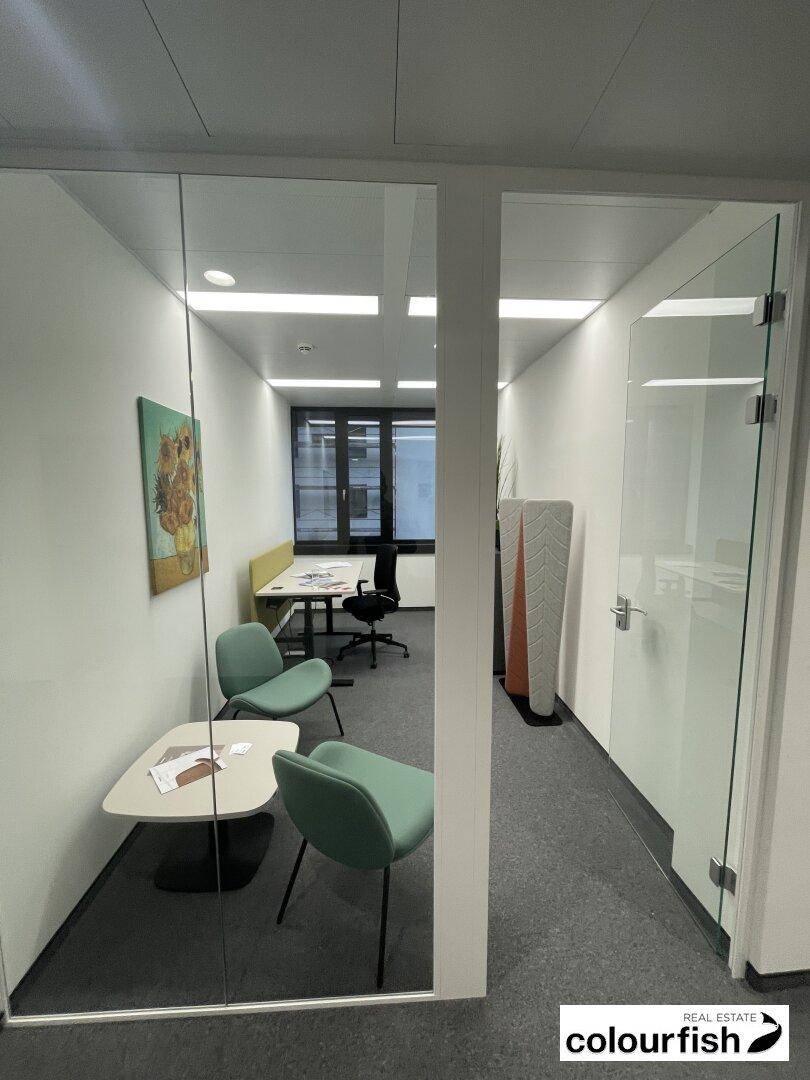Modernes Büro mit Glaswänden, Teppichboden und minimalistischer Einrichtung, ideal für konzentriertes Arbeiten.