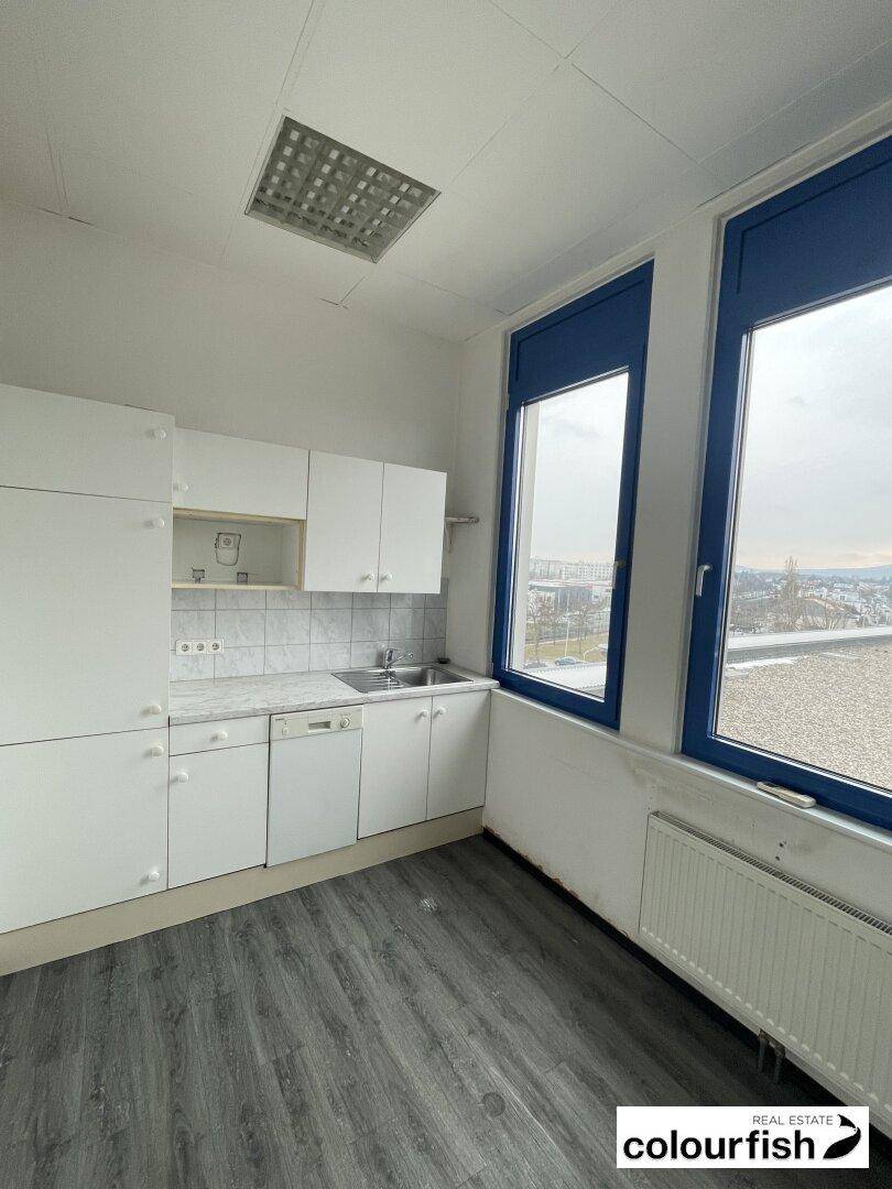 Kleine Einbauküche mit weißen Schränken, Spüle und Blick aus dem Fenster, ausgestattet mit einem Geschirrspüler.