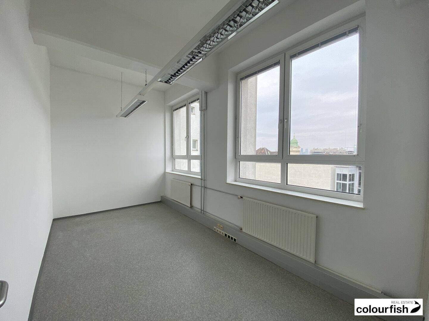Helles, leeres Büro mit zwei großen Fenstern und Heizkörpern unterhalb, bereit zur individuellen Gestaltung und Nutzung.