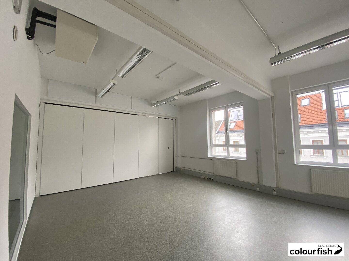 Großes Büro mit flexiblen Trennwänden und Blick auf die umliegenden Gebäude durch die Fenster, mit viel Tageslicht.
