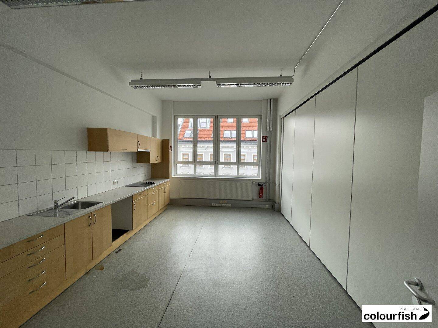 Funktionale Küche mit Holzschränken, Fliesenrückwand und einem großen Fenster, bereit zur Nutzung in einem Bürogebäude.