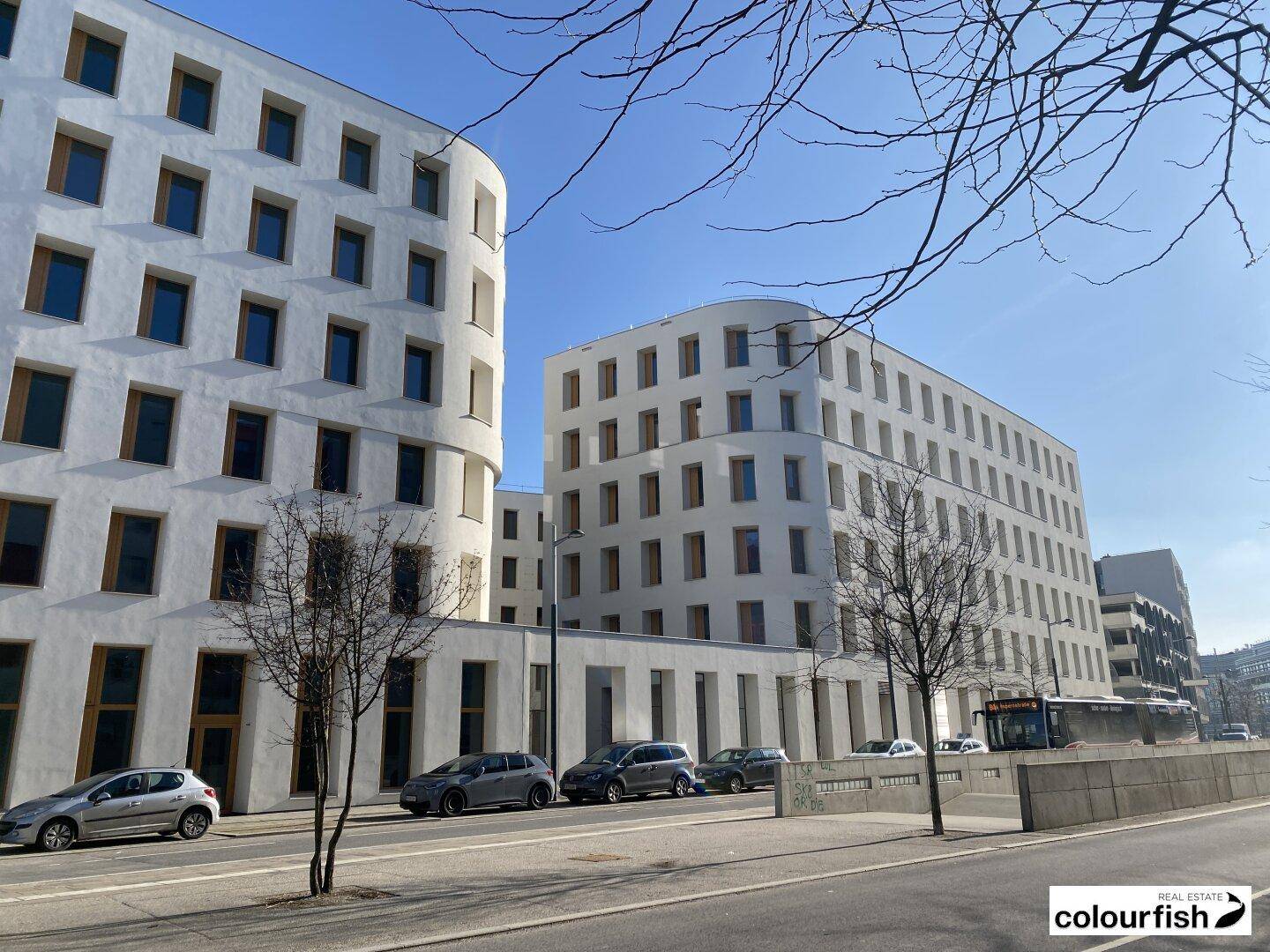 Mehrere moderne Gebäude mit weißer Fassade und vielen Fenstern entlang einer städtischen Straße.