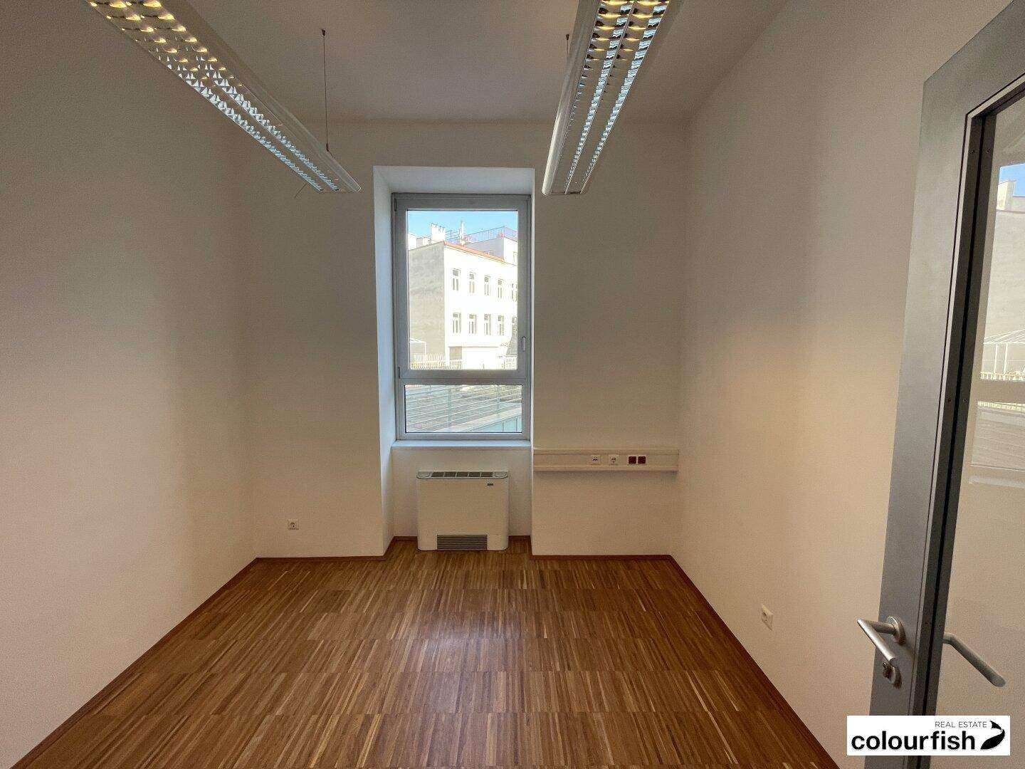 Heller Büroraum mit Holzparkettboden, weißen Wänden und Blick auf die Stadt.