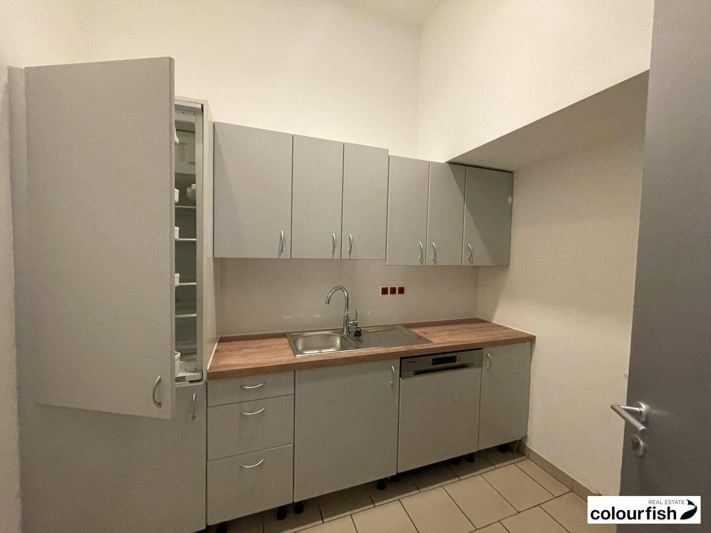Kleine, funktionale Küche mit grauen Schränken, Holzarbeitsplatte und integrierten Geräten.