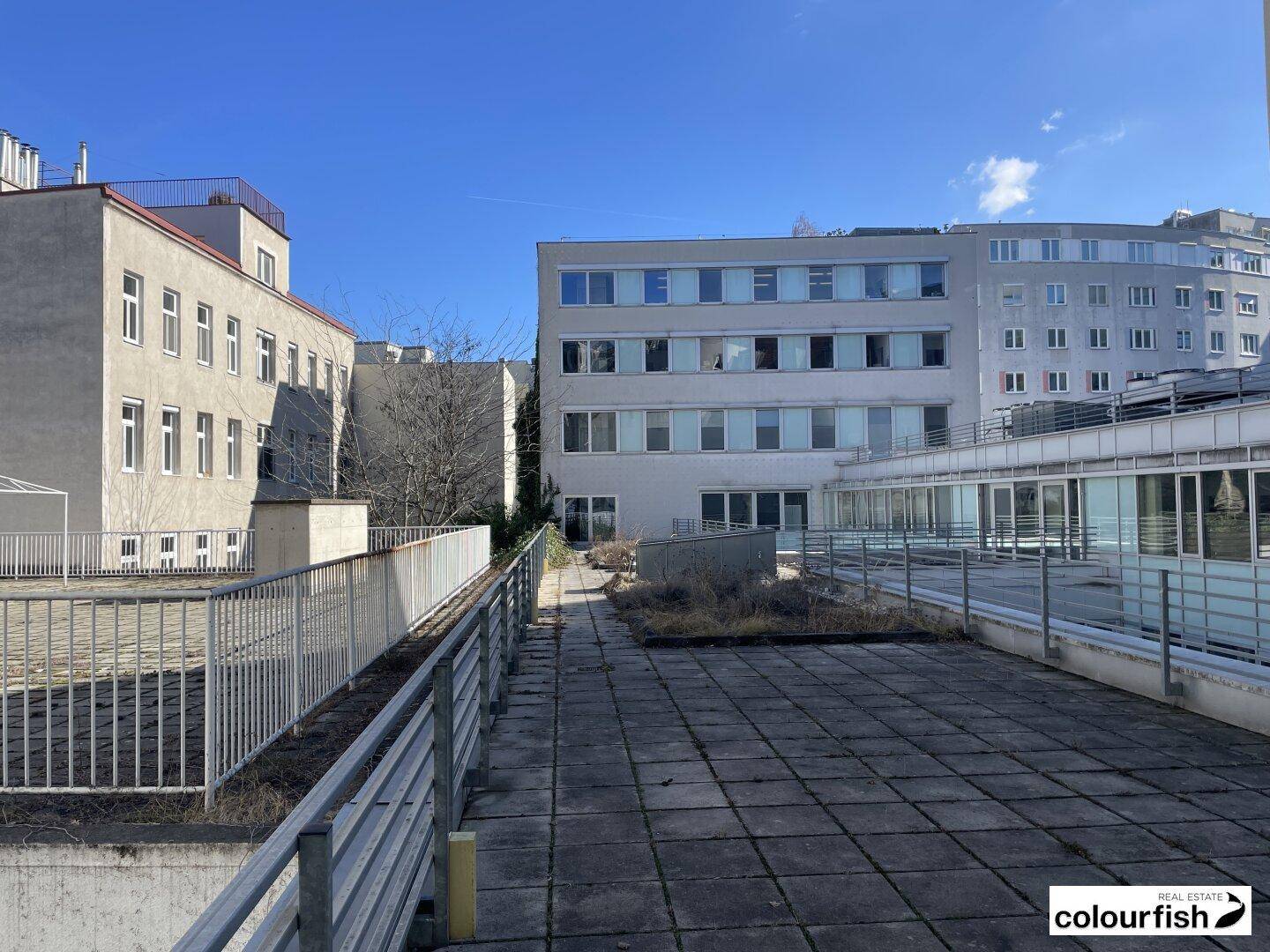 Große Dachterrasse mit weitem Blick auf umliegende Gebäude unter blauem Himmel.