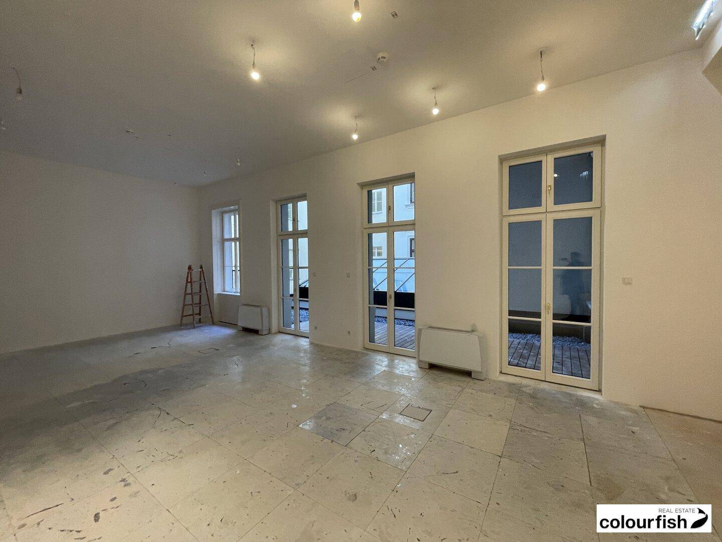 Geräumiger, leerer Raum mit großen Fenstertüren und unfertigem Boden, bereit für den Ausbau.