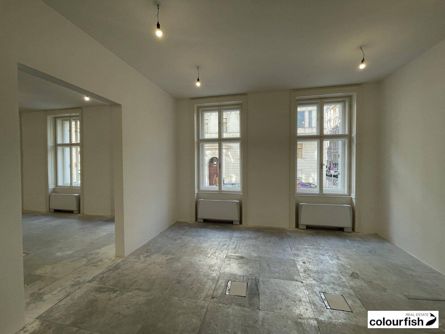 Heller Eckraum mit großen Fenstern und Betonboden, bietet viel Tageslicht.